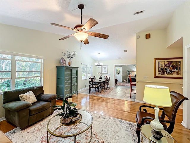 living room with ceiling fan with notable chandelier, light wood-type flooring, high vaulted ceiling, and a healthy amount of sunlight