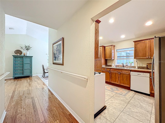 kitchen featuring white dishwasher, sink, light hardwood / wood-style flooring, stainless steel refrigerator, and lofted ceiling