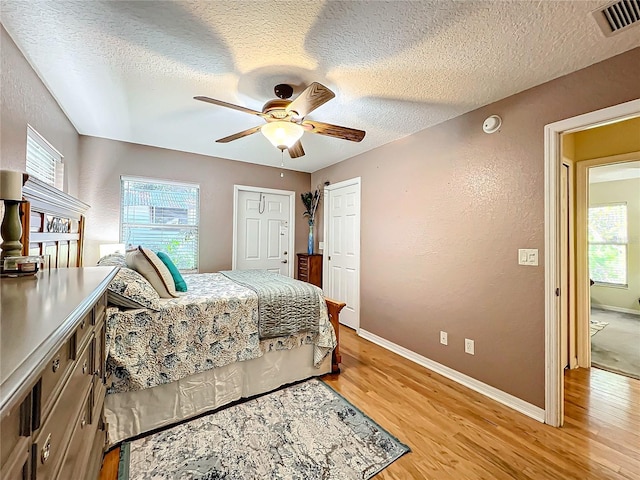 bedroom featuring multiple windows, a textured ceiling, light hardwood / wood-style floors, and ceiling fan