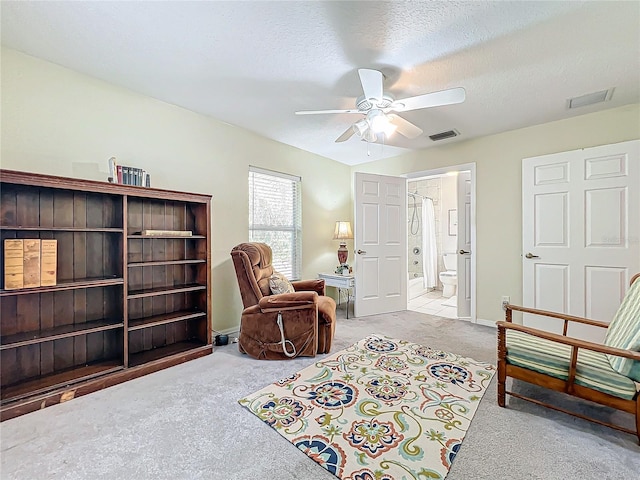 living area with light carpet, ceiling fan, and a textured ceiling