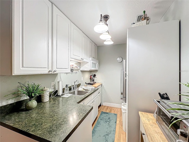 kitchen with white appliances, white cabinets, sink, light hardwood / wood-style flooring, and butcher block counters