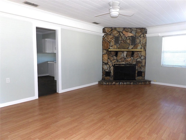 unfurnished living room with ceiling fan, wooden ceiling, a stone fireplace, hardwood / wood-style floors, and ornamental molding