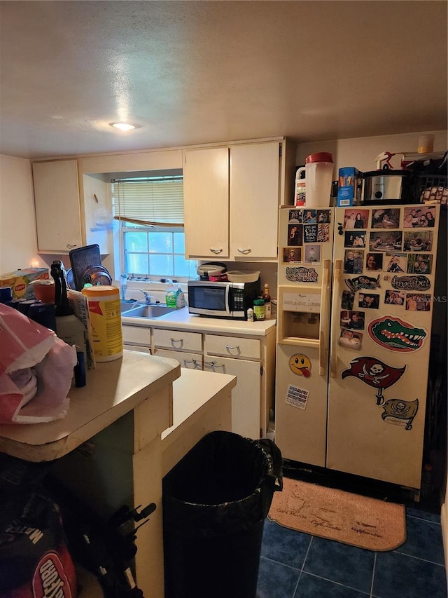 kitchen featuring dark tile patterned flooring, white cabinets, sink, white fridge with ice dispenser, and a textured ceiling