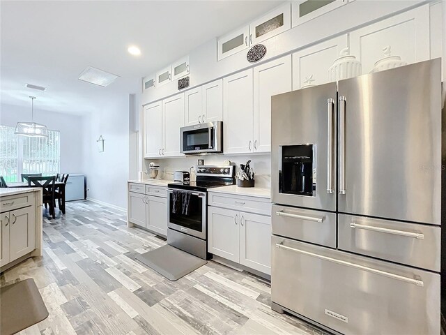 kitchen with light wood-type flooring, stainless steel appliances, white cabinetry, and hanging light fixtures