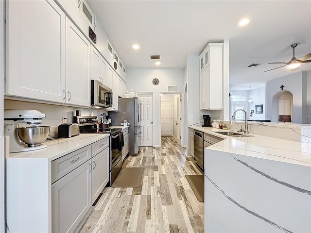 kitchen with light stone countertops, light wood-type flooring, stainless steel appliances, sink, and white cabinetry