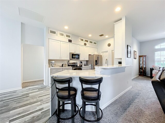 kitchen with a kitchen bar, kitchen peninsula, white cabinetry, and stainless steel appliances