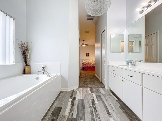 bathroom featuring hardwood / wood-style floors, vanity, a relaxing tiled tub, and ceiling fan