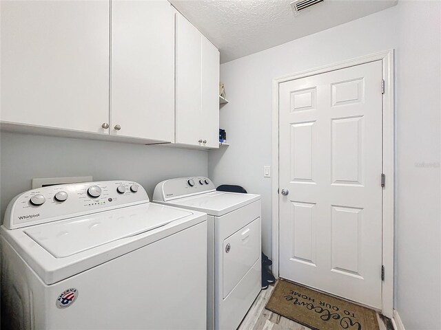 clothes washing area with light hardwood / wood-style floors, cabinets, separate washer and dryer, and a textured ceiling