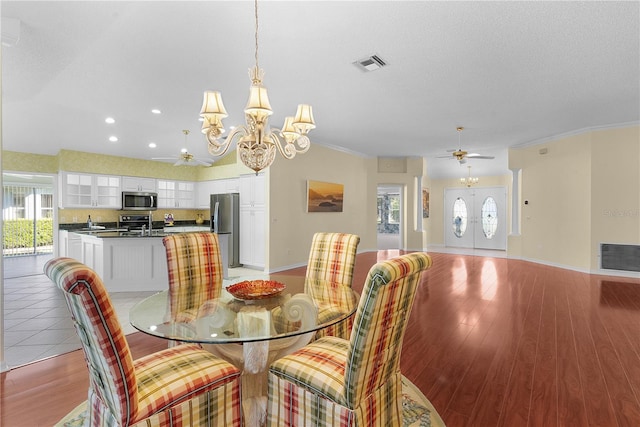 dining space featuring a textured ceiling, ceiling fan with notable chandelier, light wood-type flooring, and ornamental molding