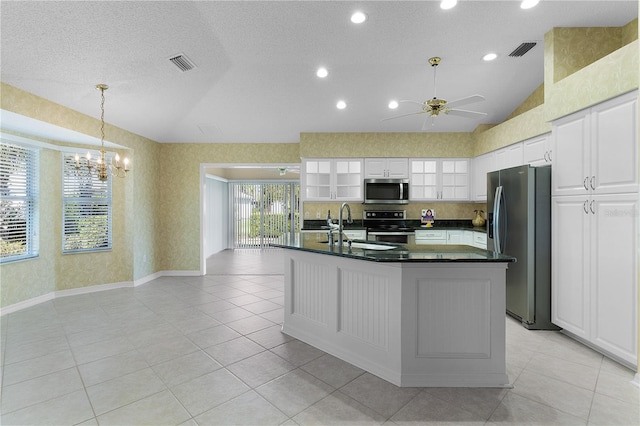 kitchen featuring white cabinets, ceiling fan with notable chandelier, a center island with sink, vaulted ceiling, and appliances with stainless steel finishes