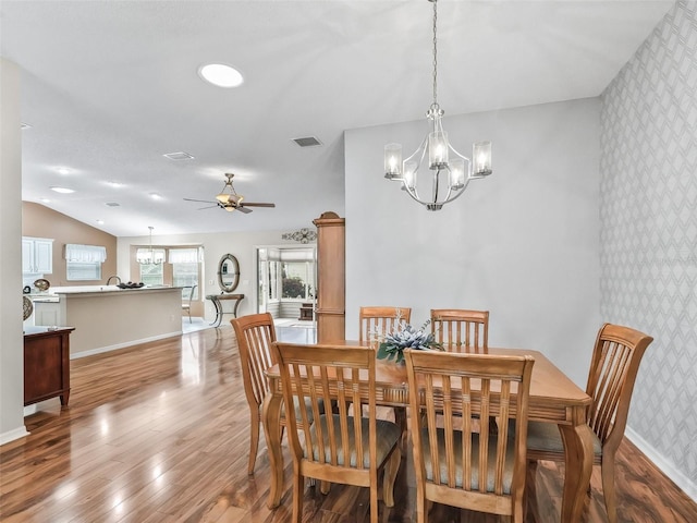 dining room with ceiling fan with notable chandelier, lofted ceiling, and light wood-type flooring