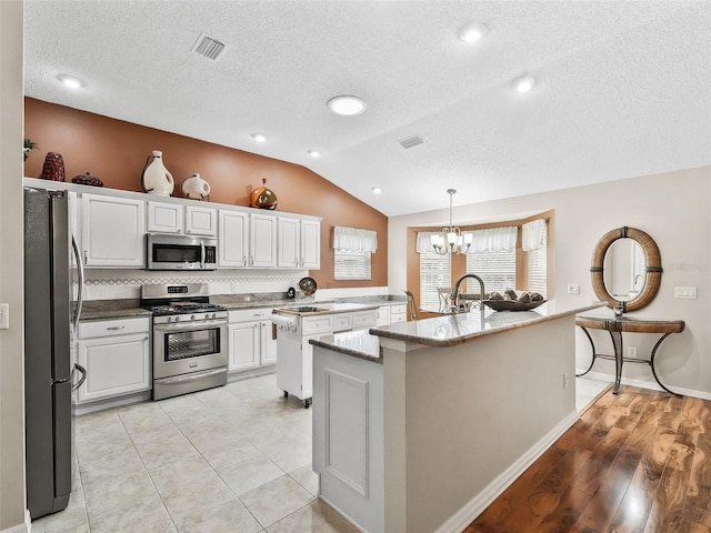 kitchen featuring white cabinets, lofted ceiling, decorative light fixtures, stainless steel appliances, and a kitchen island with sink