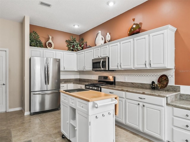 kitchen featuring white cabinetry, butcher block counters, appliances with stainless steel finishes, decorative backsplash, and a center island