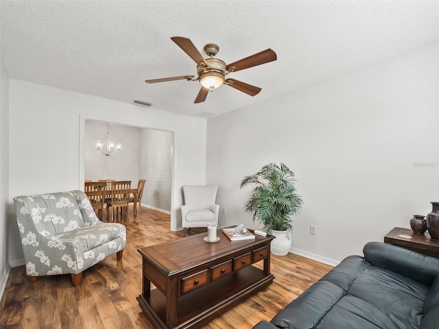 living room featuring ceiling fan with notable chandelier, wood-type flooring, and a textured ceiling