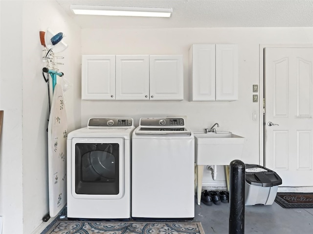 clothes washing area with cabinets, a textured ceiling, sink, and washing machine and clothes dryer