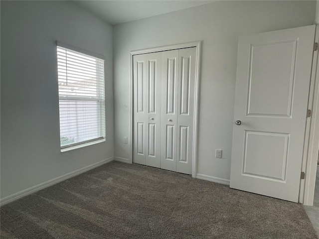 unfurnished bedroom featuring multiple windows, dark carpet, and a closet