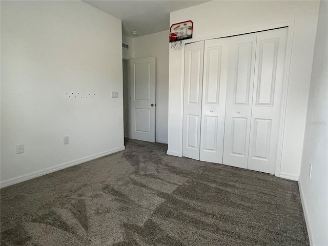 unfurnished bedroom with dark colored carpet and a closet