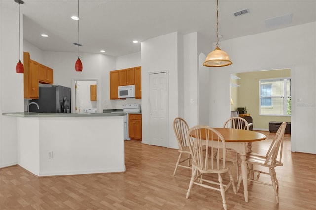 kitchen featuring kitchen peninsula, white appliances, light hardwood / wood-style floors, and hanging light fixtures