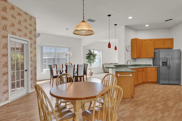 kitchen with kitchen peninsula, a healthy amount of sunlight, hanging light fixtures, and stainless steel refrigerator with ice dispenser