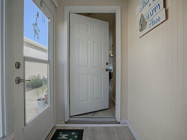 doorway with light hardwood / wood-style flooring, a wealth of natural light, and wooden walls