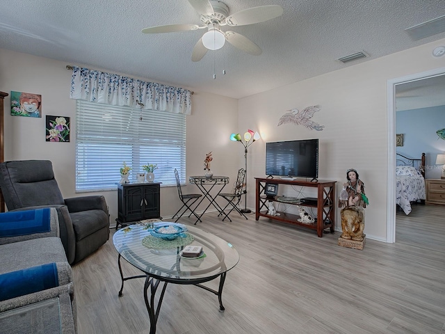 living room with ceiling fan, light hardwood / wood-style flooring, and a textured ceiling