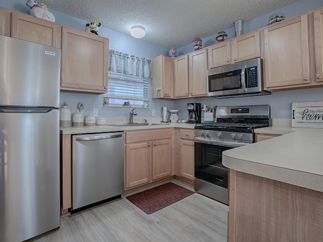 kitchen with sink, stainless steel appliances, a textured ceiling, light brown cabinetry, and light wood-type flooring