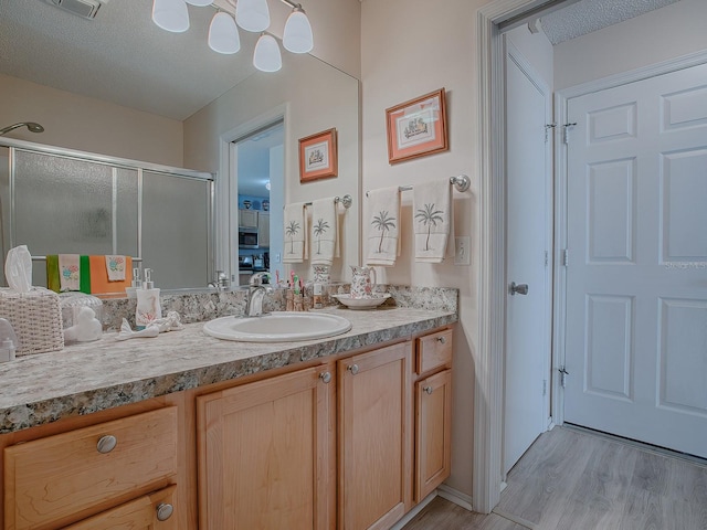 bathroom featuring hardwood / wood-style floors, vanity, a shower with door, and a textured ceiling