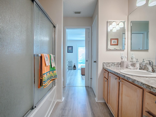 bathroom with hardwood / wood-style flooring, vanity, shower / bath combination with glass door, and a textured ceiling