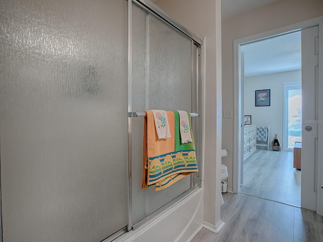 bathroom with wood-type flooring, a textured ceiling, toilet, and bath / shower combo with glass door