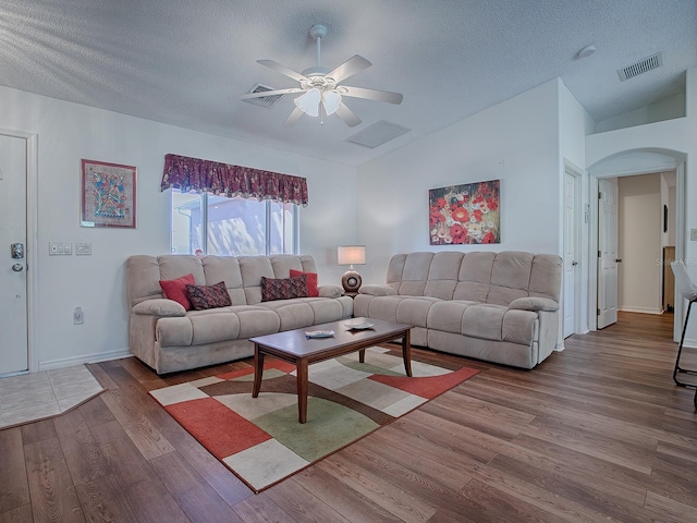 living room with wood-type flooring, a textured ceiling, vaulted ceiling, and ceiling fan