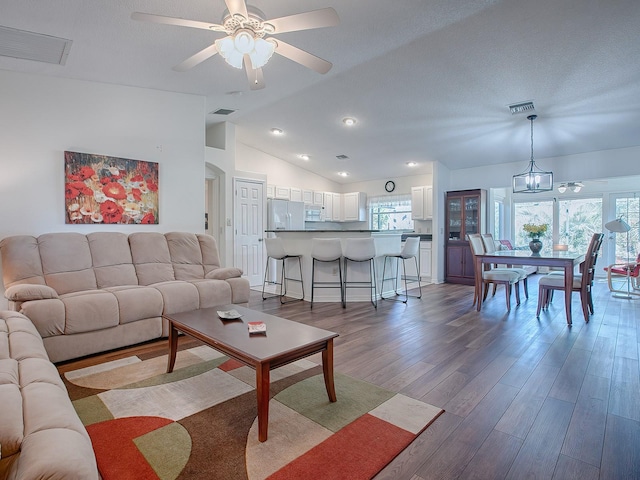 living room with ceiling fan with notable chandelier, wood-type flooring, lofted ceiling, and a textured ceiling