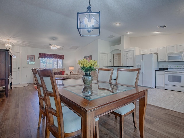 dining space with a textured ceiling, light hardwood / wood-style flooring, ceiling fan with notable chandelier, and lofted ceiling