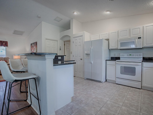 kitchen featuring a kitchen breakfast bar, white appliances, white cabinetry, lofted ceiling, and light tile patterned flooring