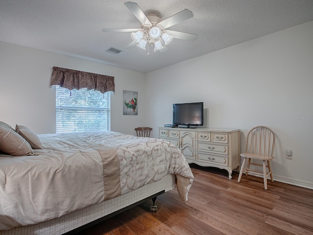 bedroom with ceiling fan, wood-type flooring, and a textured ceiling