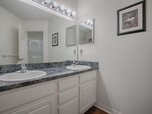 bathroom with a textured ceiling, vanity, and walk in shower