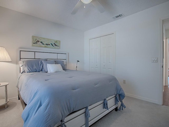 bedroom featuring a textured ceiling, a closet, ceiling fan, and light colored carpet