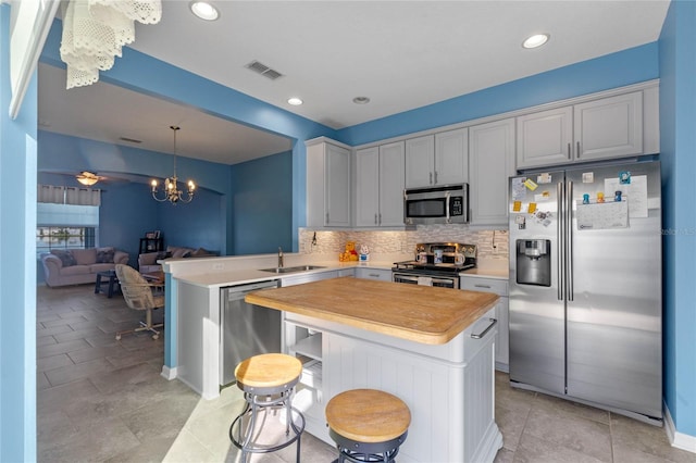 kitchen with ceiling fan with notable chandelier, stainless steel appliances, a peninsula, visible vents, and backsplash