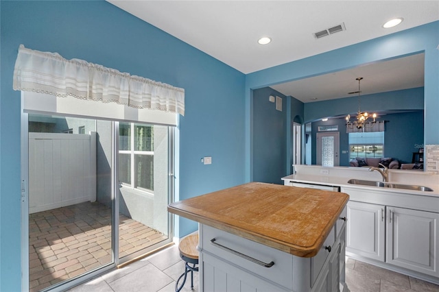 kitchen with a notable chandelier, a kitchen island, a sink, visible vents, and hanging light fixtures