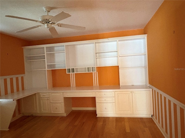 unfurnished office featuring ceiling fan, light hardwood / wood-style flooring, built in desk, and a textured ceiling