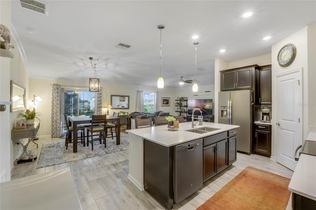 kitchen featuring stainless steel appliances, decorative light fixtures, a center island with sink, ceiling fan with notable chandelier, and light wood-type flooring