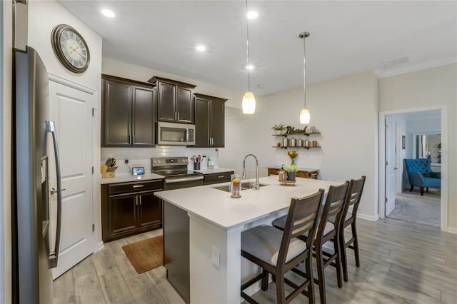 kitchen with a breakfast bar, light wood-type flooring, an island with sink, appliances with stainless steel finishes, and decorative light fixtures