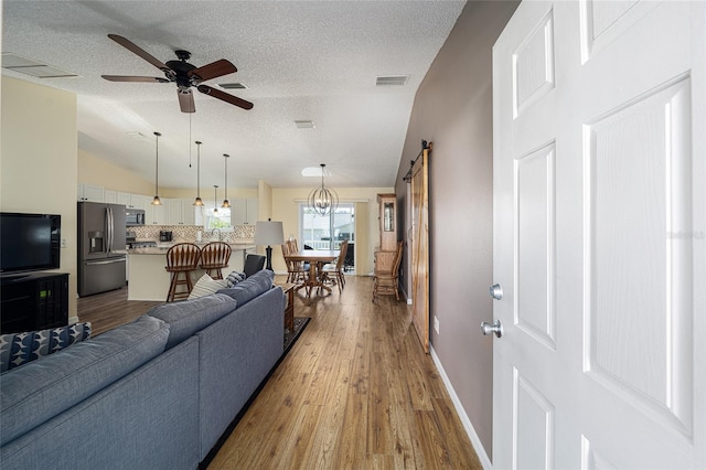 living room with ceiling fan, a barn door, hardwood / wood-style floors, a textured ceiling, and lofted ceiling