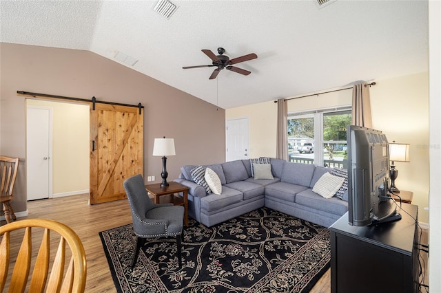 living room featuring ceiling fan, a barn door, light hardwood / wood-style floors, a textured ceiling, and vaulted ceiling