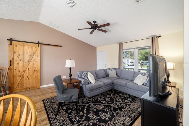 living room with ceiling fan, a barn door, a textured ceiling, lofted ceiling, and light wood-type flooring