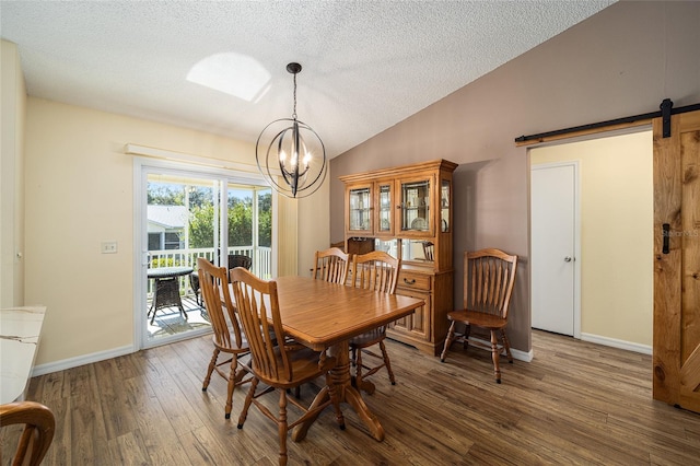 dining area featuring a textured ceiling, dark wood-type flooring, a barn door, a chandelier, and lofted ceiling