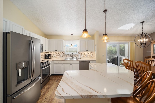 kitchen with white cabinetry, sink, stainless steel appliances, pendant lighting, and a kitchen island