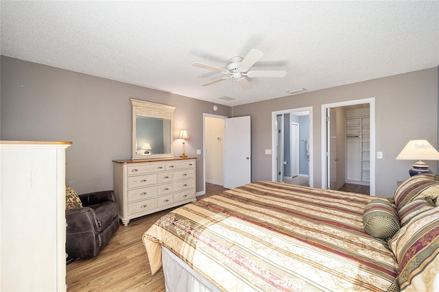 bedroom featuring a walk in closet, a textured ceiling, ceiling fan, light hardwood / wood-style floors, and a closet