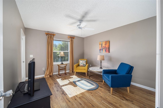 living area with ceiling fan, wood-type flooring, and a textured ceiling