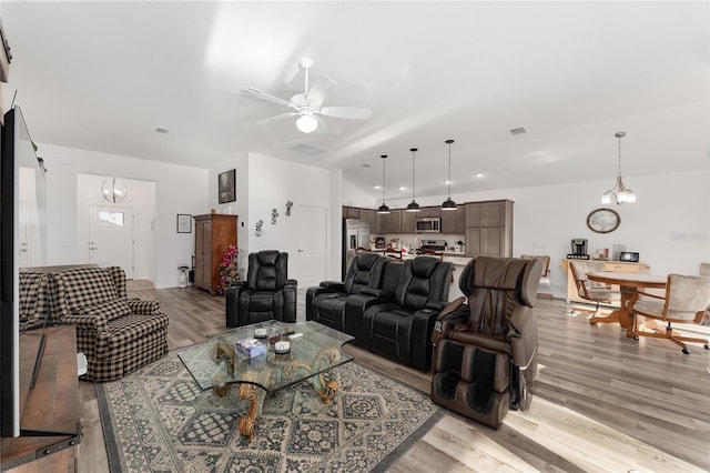 living room featuring ceiling fan with notable chandelier and light hardwood / wood-style floors