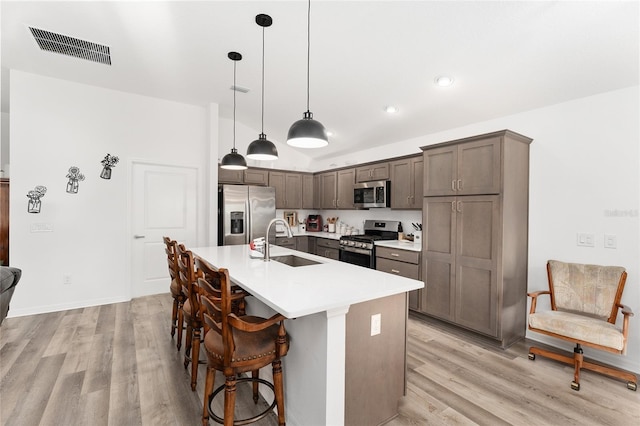 kitchen with pendant lighting, sink, stainless steel appliances, and light hardwood / wood-style flooring